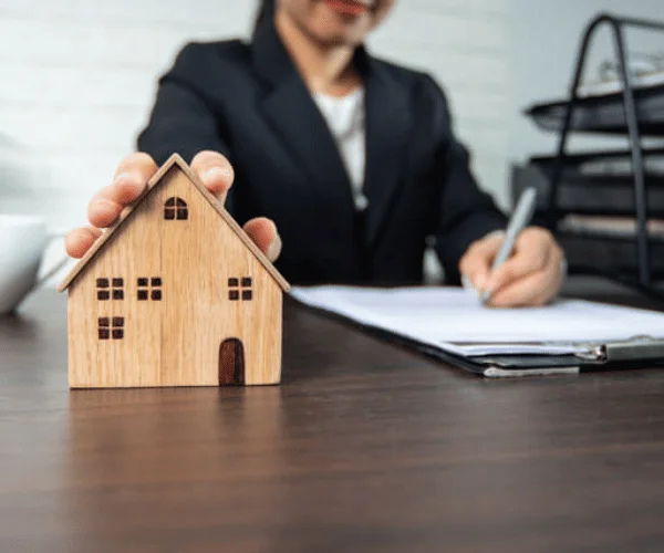 Real estate professional reviewing documents while holding a wooden house model, representing residential property appraisal and valuation services