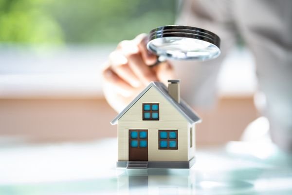 Close-up of a miniature house model being examined with a magnifying glass, representing a residential property appraisal or home inspection process.